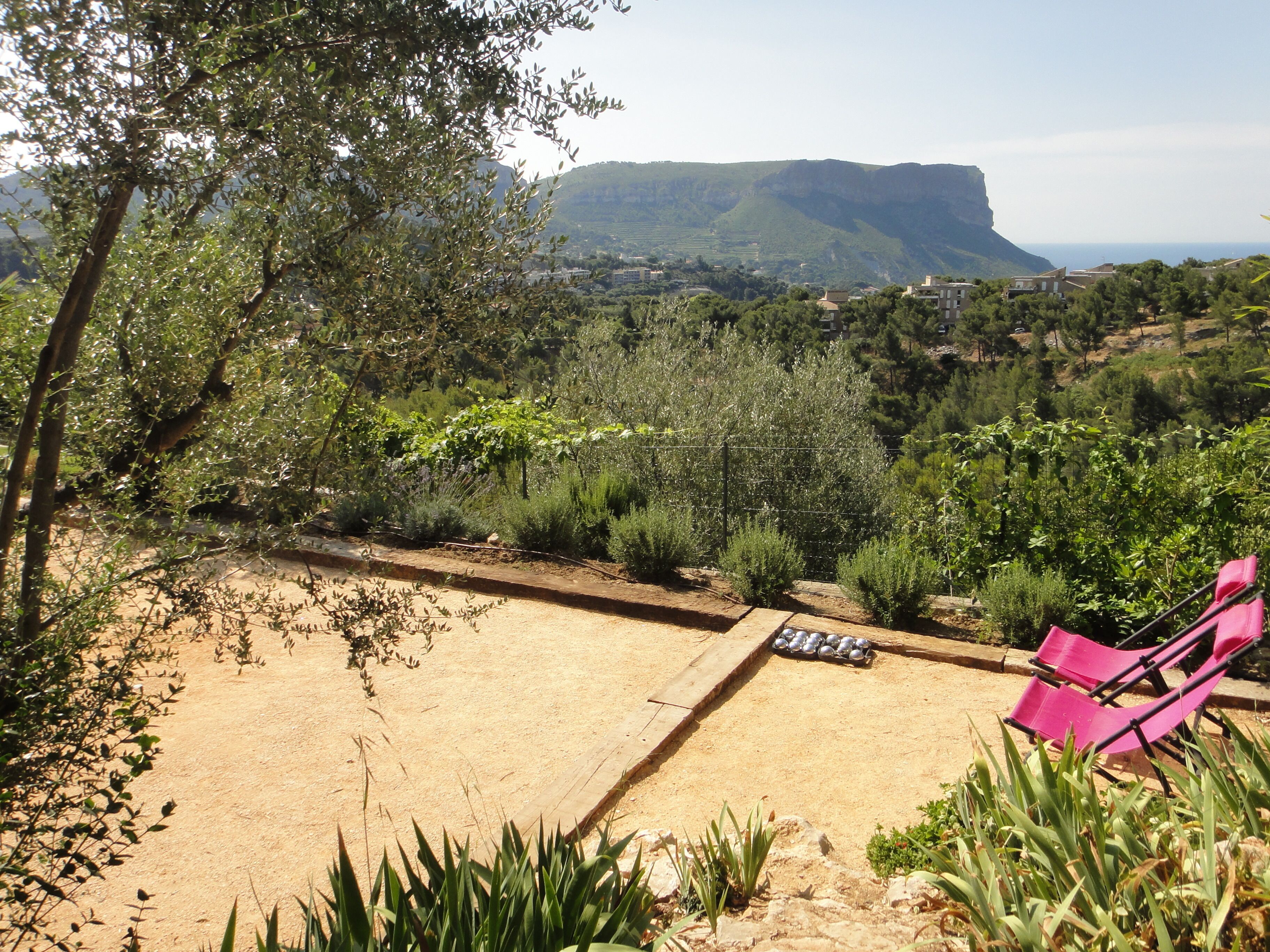 Un jardín con un sendero de tierra, una silla rosa y vistas a un paisaje montañoso.