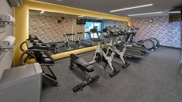 A gym with cardio machines, weight benches, and a mirrored wall.