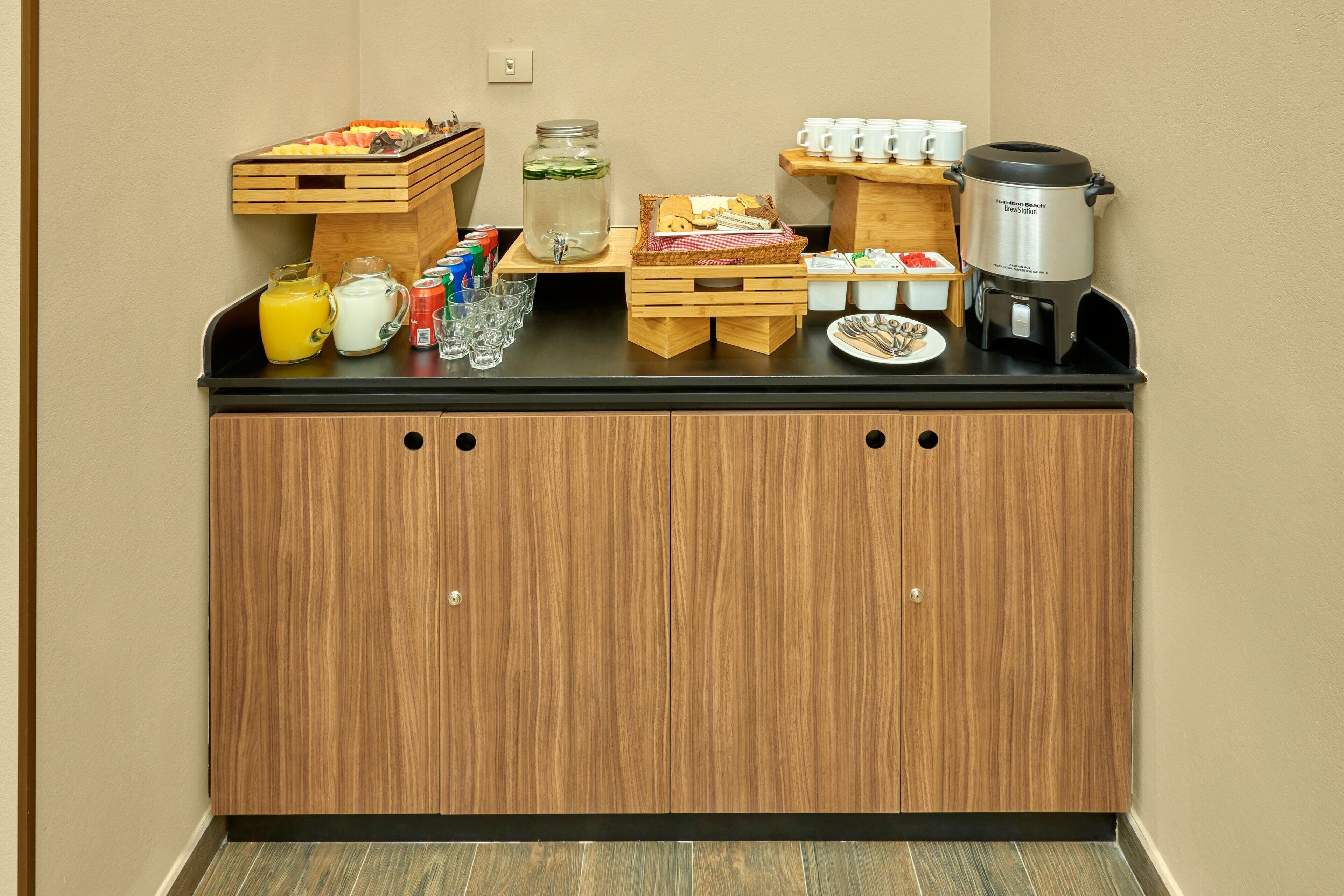 A breakfast bar with a coffee maker, fruit, and beverages.