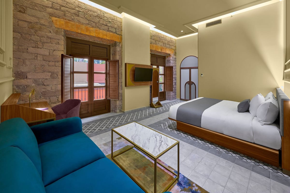 A hotel room with a bed, a sofa, a TV, and a brick wall.