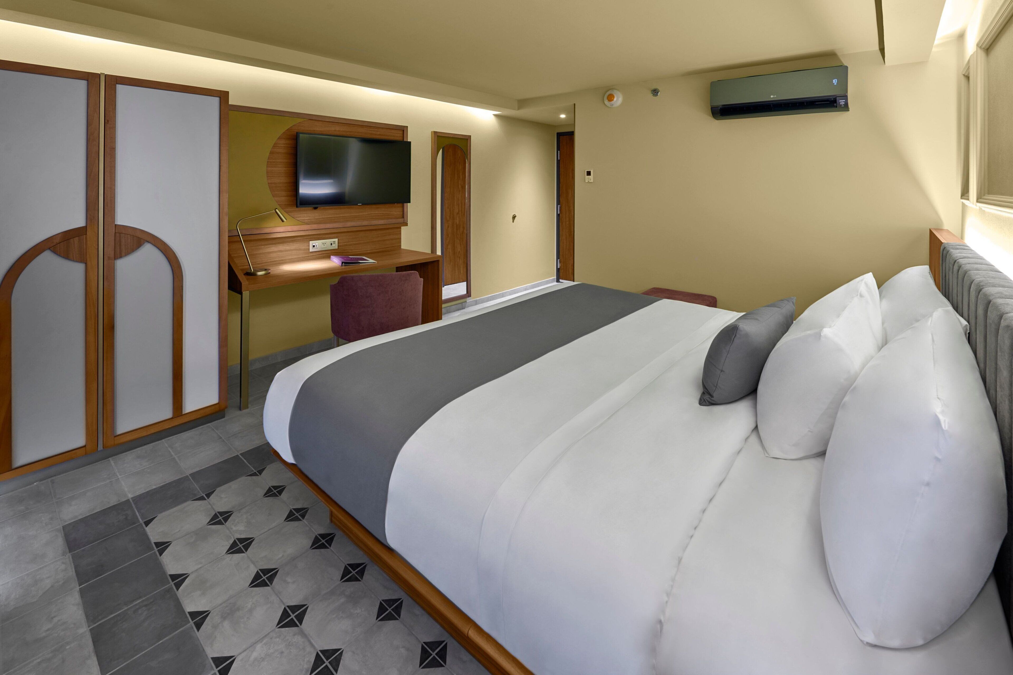 Habitación de hotel con una cama grande, un escritorio con televisor y un equipo de aire acondicionado.