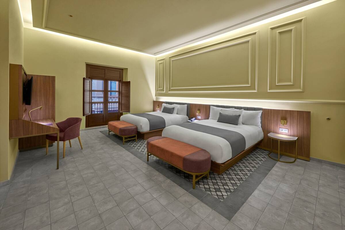 A modern hotel room with two beds, a desk, a chair, and a small table.