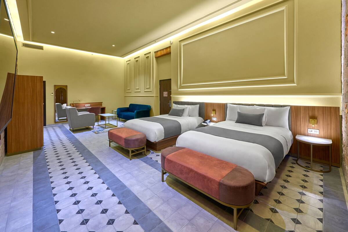 A hotel room with two beds, a desk, a chair, and a small table.