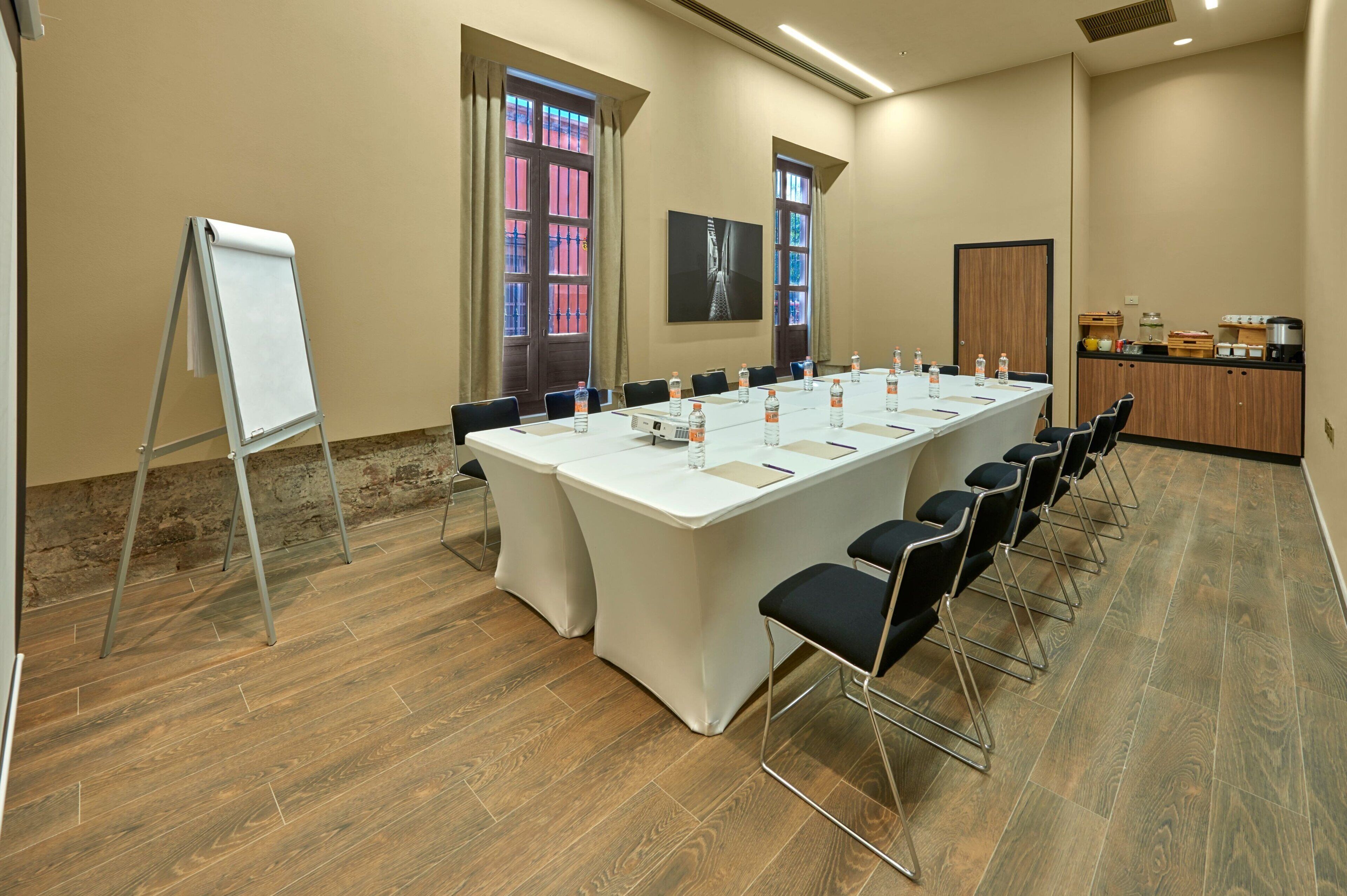 Un salón de conferencias con una larga mesa, sillas, una pizarra y una zona de cocina.
