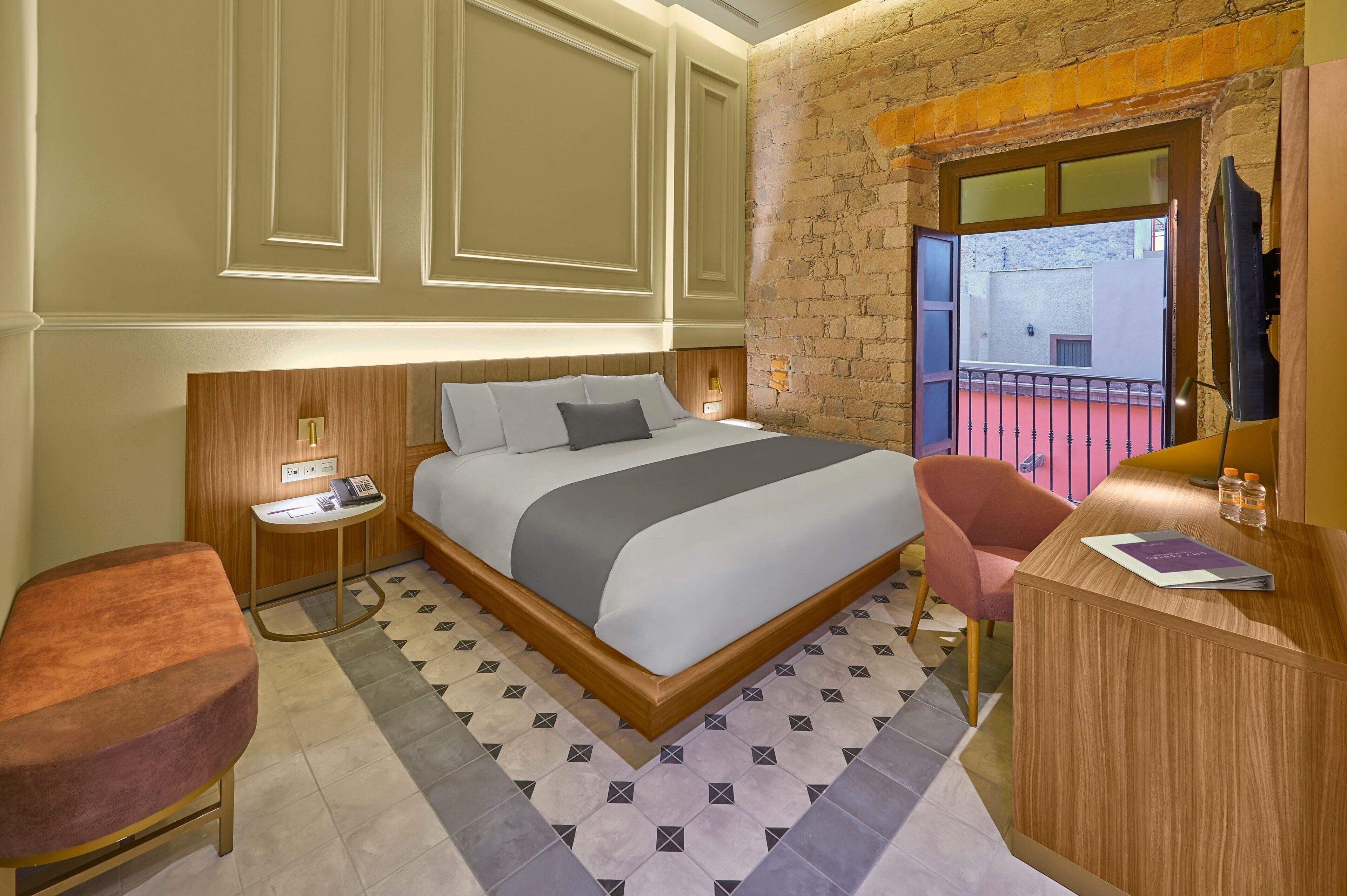 A hotel room with a bed, a desk, a chair, a nightstand, and a window with a view.