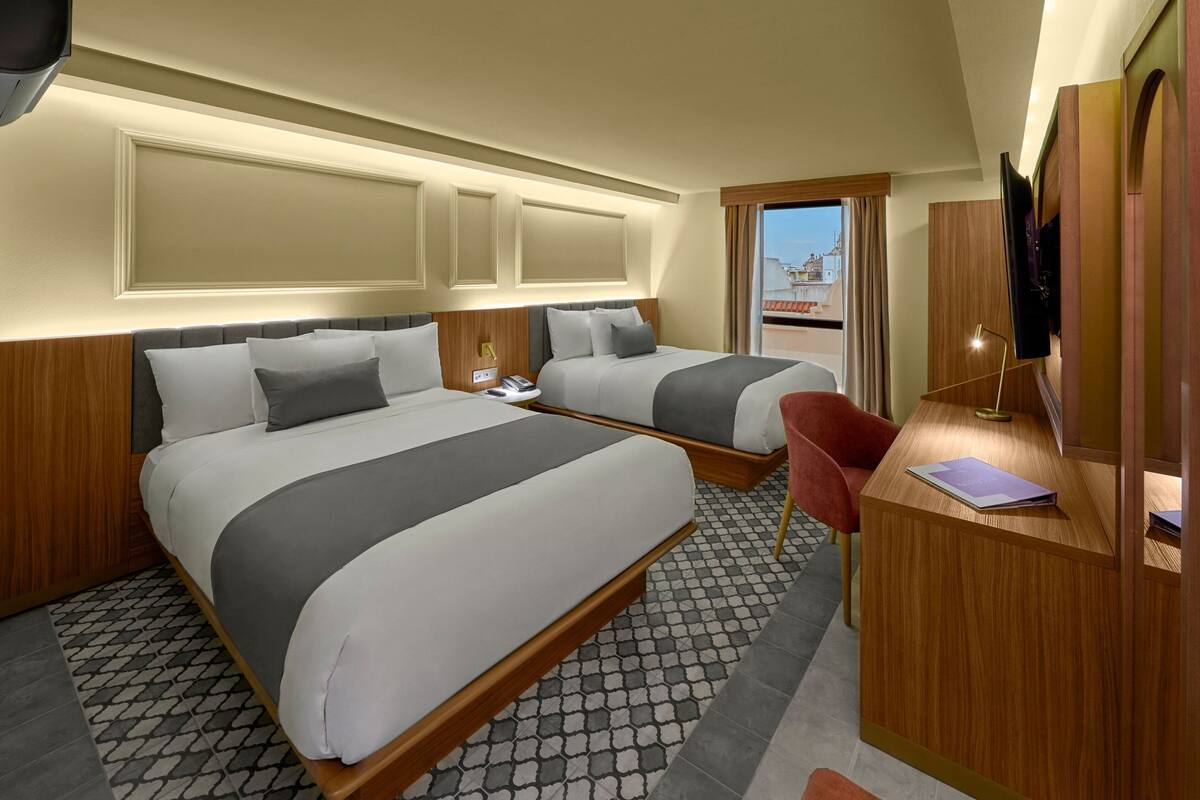 A hotel room with two beds, a desk, a chair, and a TV.