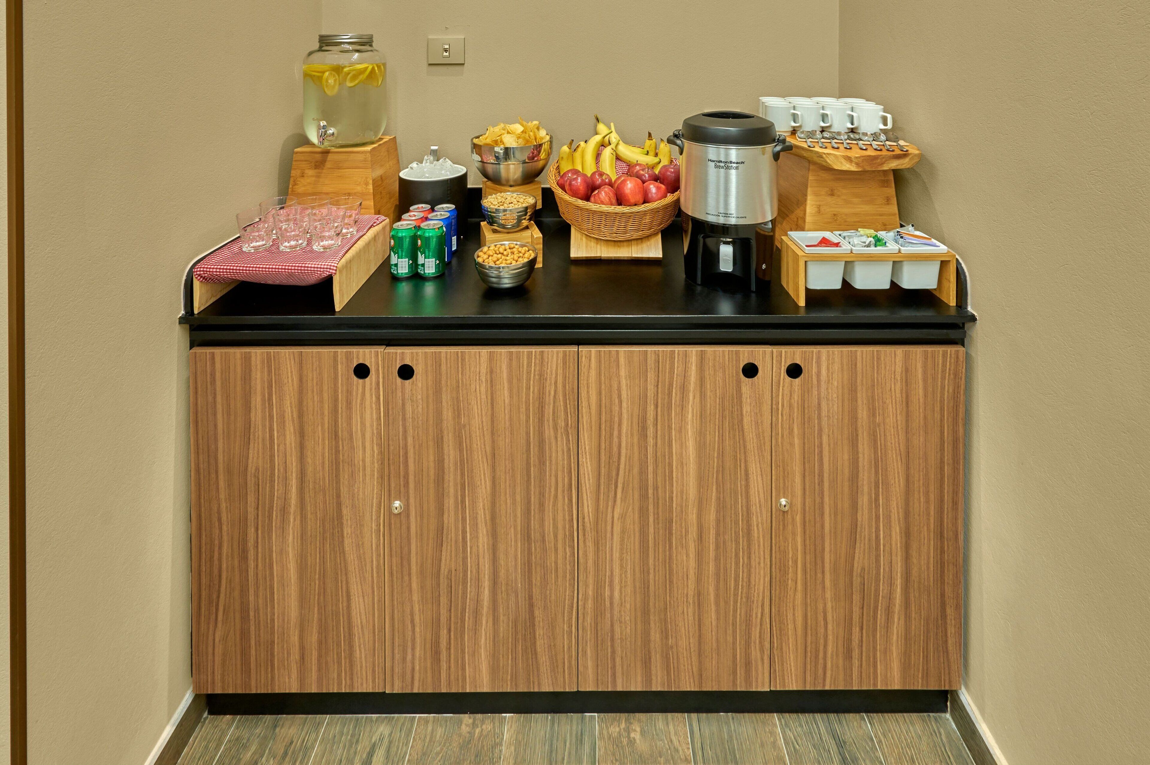 A breakfast bar with a variety of food and drink options, including fruits, cereals, and coffee.