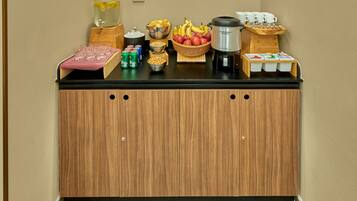 A breakfast bar with a variety of food and drink options, including fruits, cereals, and coffee.