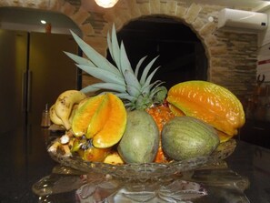 A fruit bowl on a glass stand with a stone wall and a door in the background. - Villa Man Cina (Capesterre-Belle-Eau)