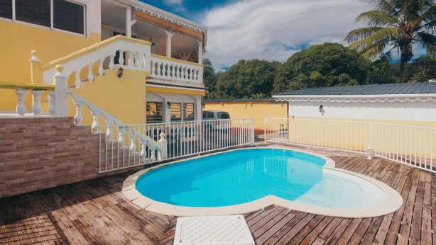 Una terraza de madera con piscina, barandilla blanca y un edificio de dos pisos con balcones.