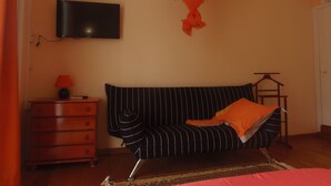 A room with a black-striped sofa, a television mounted on the wall, a wooden dresser, and a hanging orange decorative piece. - Villa Man Cina (Capesterre-Belle-Eau)