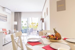 A hotel room with a dining area, a sofa, a TV, and a view of palm trees. - Beachfront apartment in El Duque (Costa Adeje)
