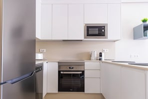 A modern kitchen with white cabinetry, a built-in microwave, a stove, and an oven. - Beachfront apartment in El Duque (Costa Adeje)