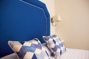 A bed with a blue headboard, two patterned pillows, and a wall-mounted light fixture. - Hotel Boutique Tao Caleta Mar (La Oliva)