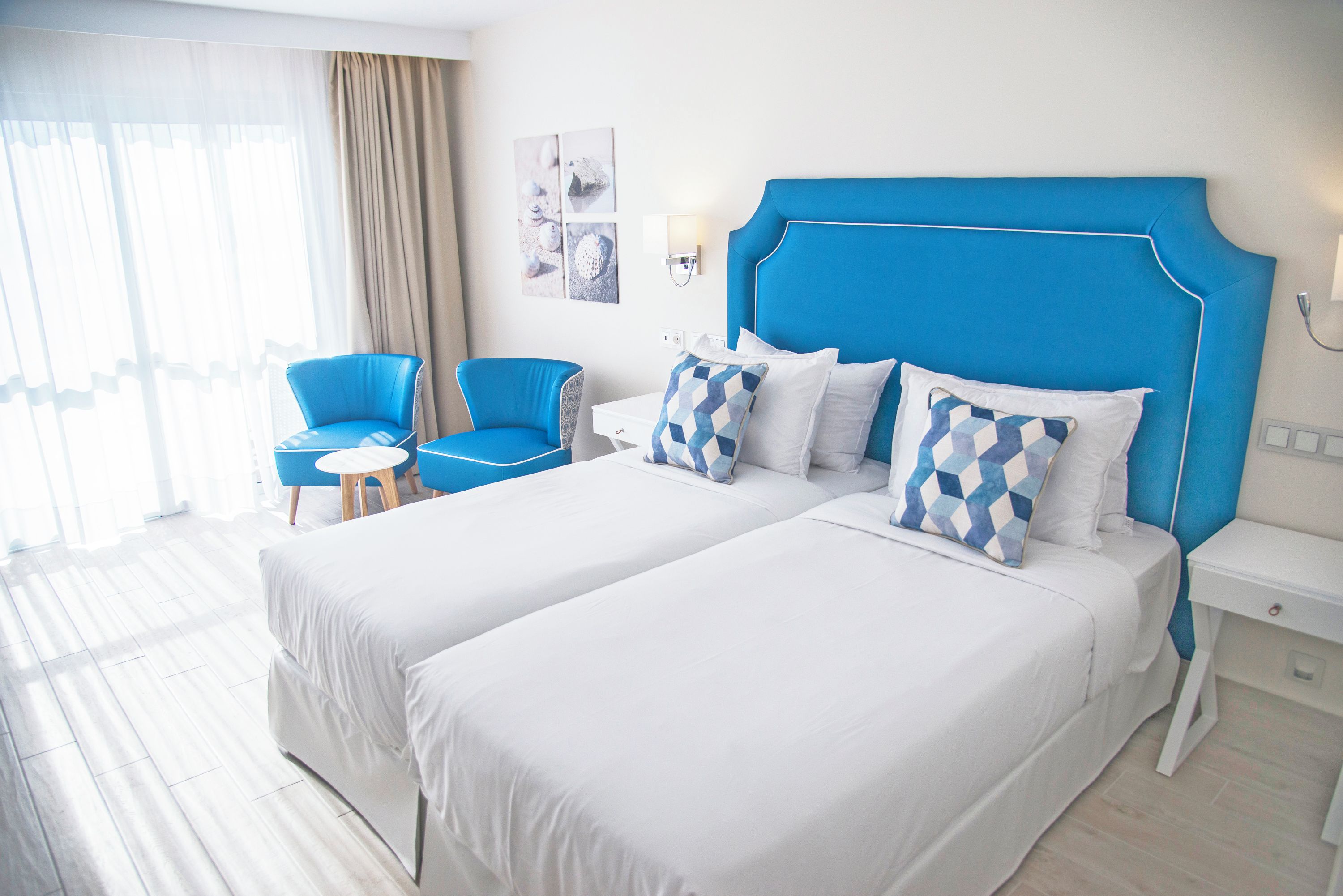 Una camera d'albergo con due letti, una testiera blu, un tavolino e una sedia.