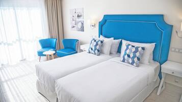Una camera d'albergo con due letti, una testiera blu, un tavolino e una sedia.