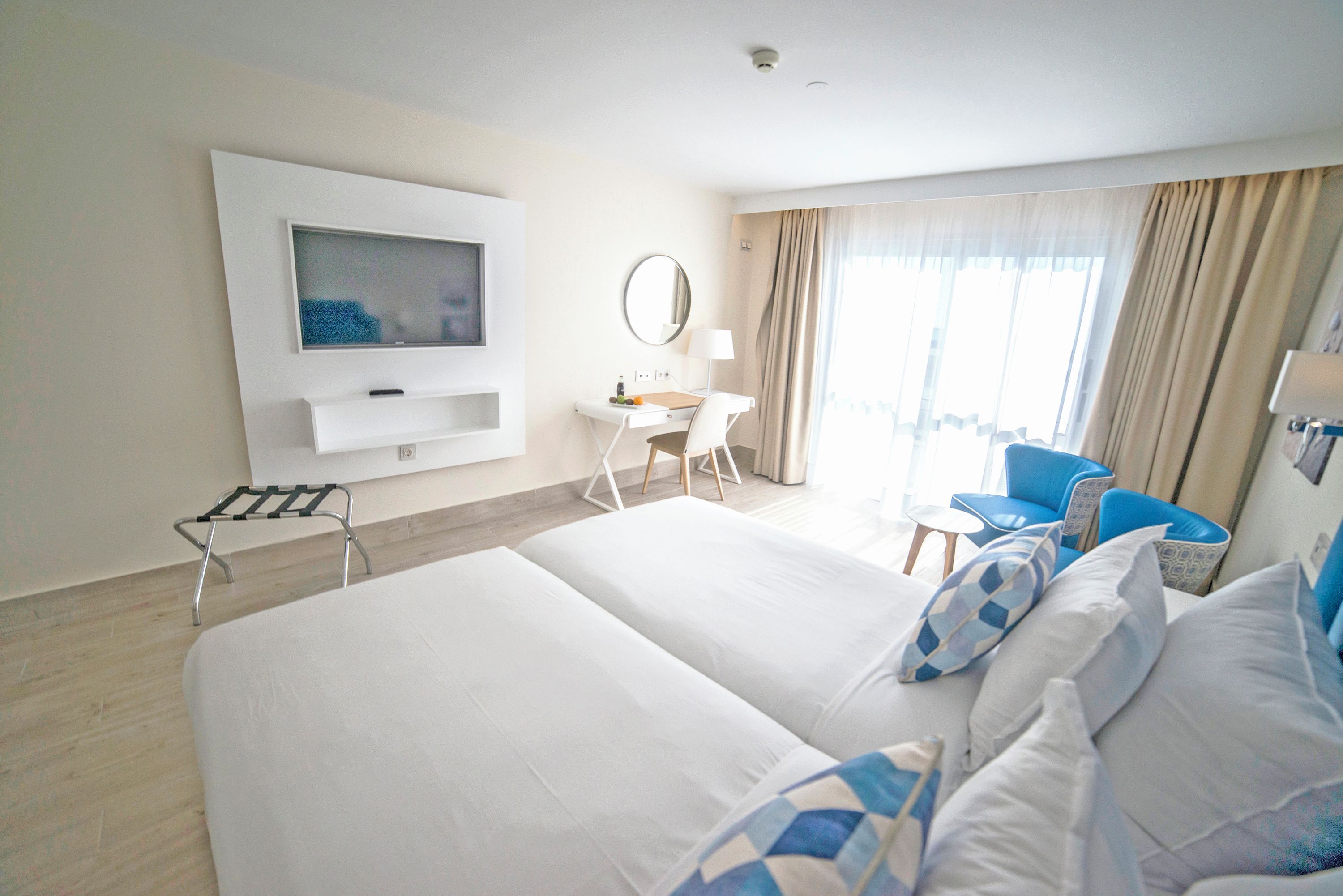 Hotelkamer met een groot bed, een bureau met stoel, een aan de muur bevestigde televisie en een raam met gordijnen.