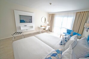 A hotel room with a large bed, a desk with a chair, a TV mounted on the wall, and a window with curtains. - Hotel Boutique Tao Caleta Mar (La Oliva)