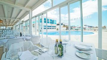 Un restaurant doté d’une terrasse offrant une vue sur une piscine et sur un bâtiment à la façade bleue.