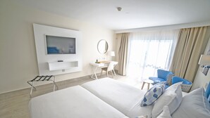 A hotel room with a large bed, a desk with a chair, a TV mounted on the wall, and a window with curtains. - Hotel Boutique Tao Caleta Mar (La Oliva)