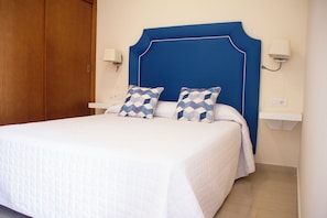 A bedroom with a bed, two pillows, a nightstand, a wall-mounted lamp, and a wooden wardrobe. - Hotel Boutique Tao Caleta Mar (La Oliva)