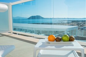 A balcony with a table holding fruits and a glass railing overlooking a coastal landscape. - Hotel Boutique Tao Caleta Mar (La Oliva)