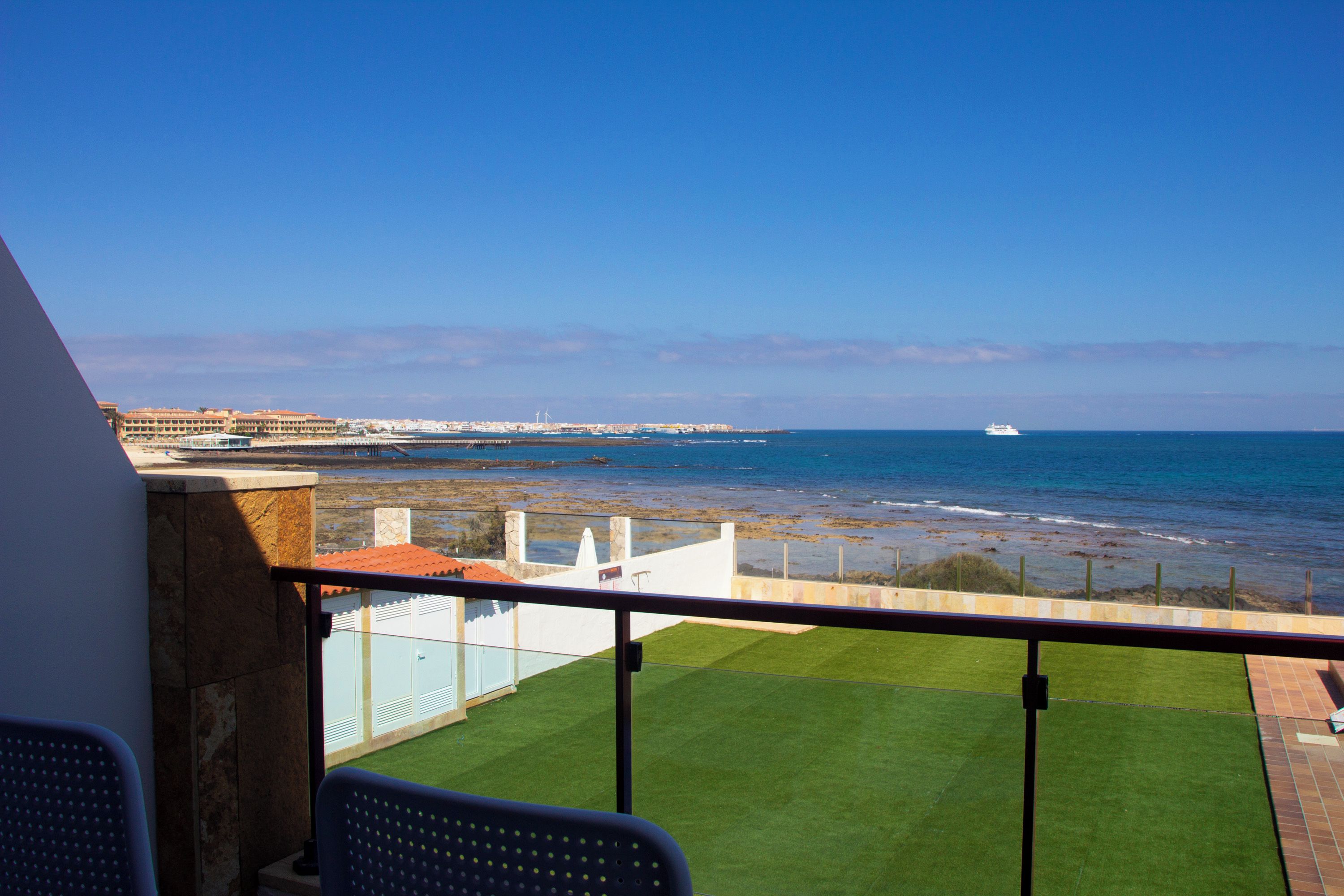 A balcony with a view of the sea, a grassy area, and a distant cityscape.