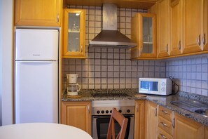 A kitchen with wooden cabinets, a stainless steel range hood, a microwave, and a built-in oven. - Hotel Boutique Tao Caleta Mar (La Oliva)