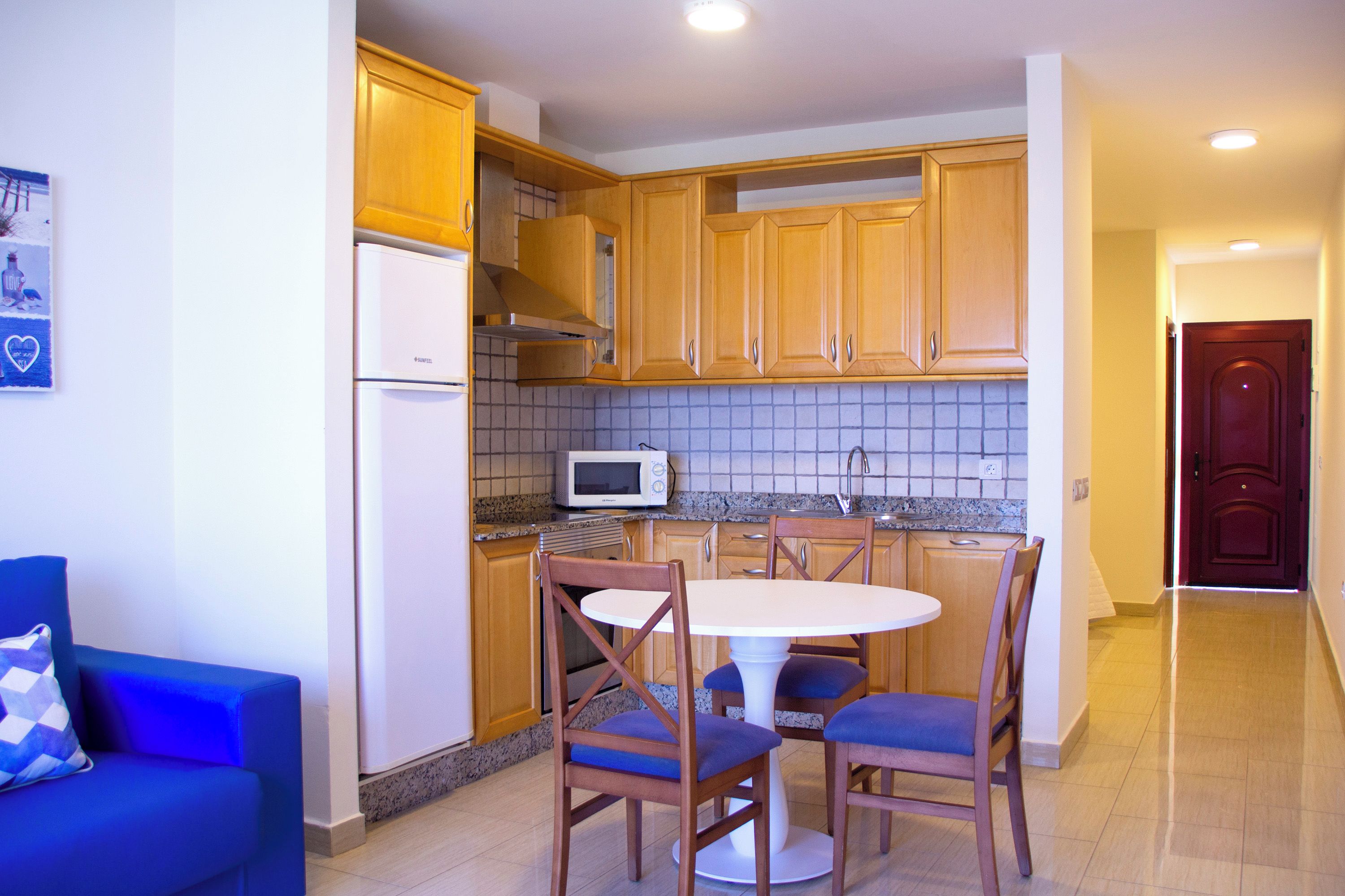 Una cucina compatta con mobili in legno, un frigorifero, un forno a microonde e un tavolo con sedie.