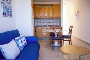 A compact living space with a kitchenette, a dining area with a table and chairs, and a sofa with a patterned cushion.