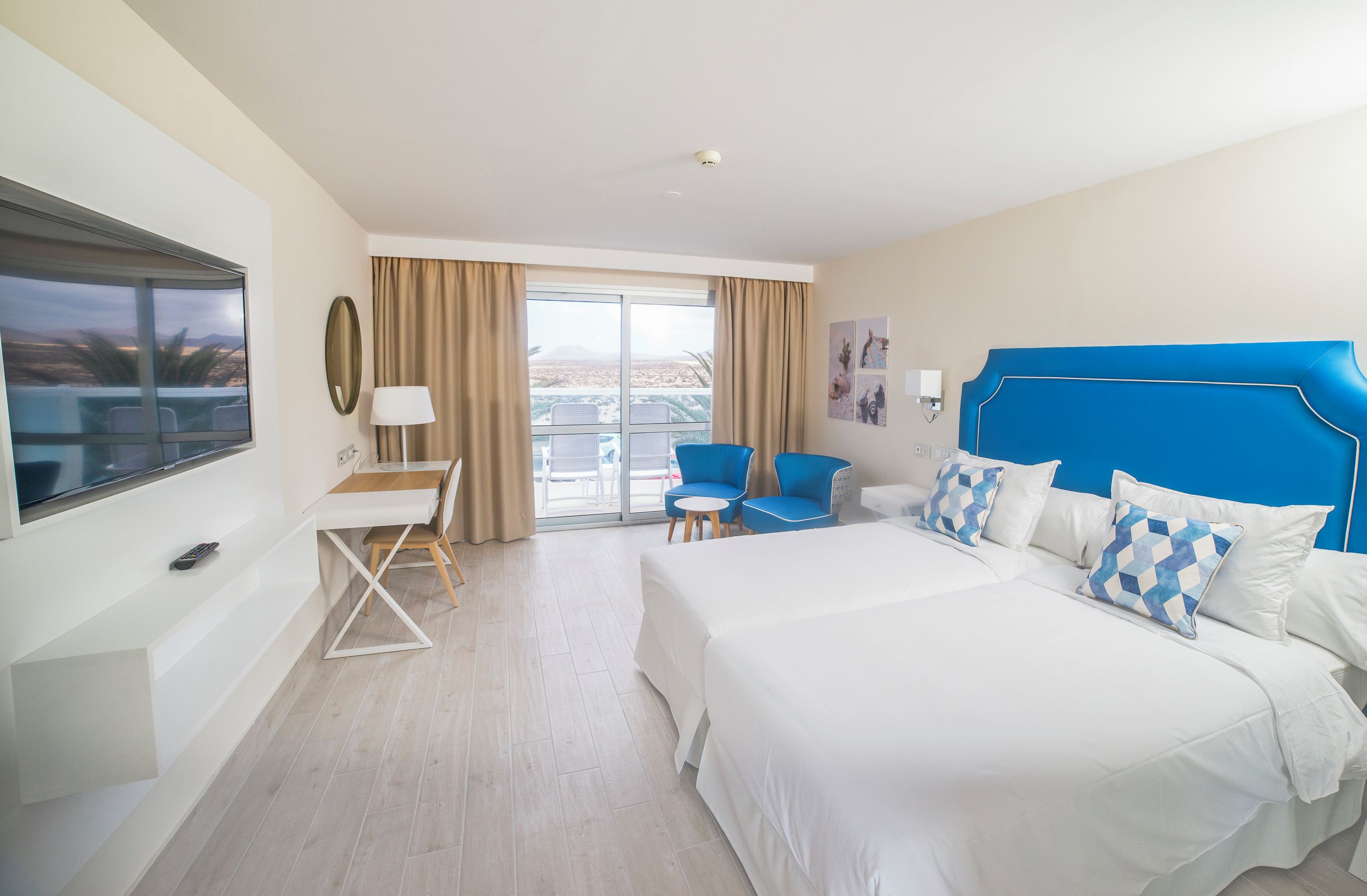 Ein Hotelzimmer mit einem großen Bett, einem Schreibtisch, einem Sessel, einem Fernseher und einem Balkon mit Blick.