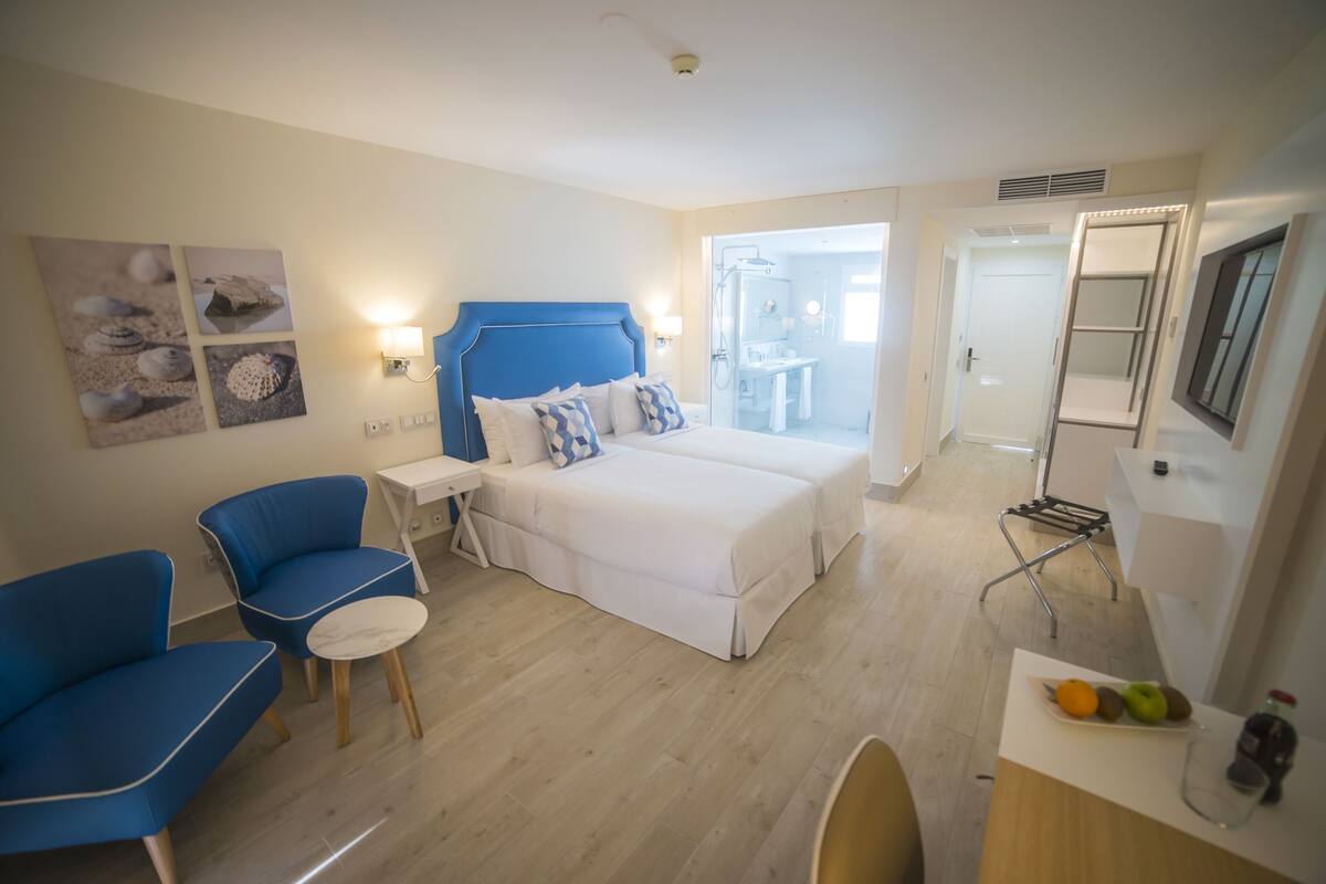 A hotel room with a bed, a desk, a chair, a small table, and a TV.