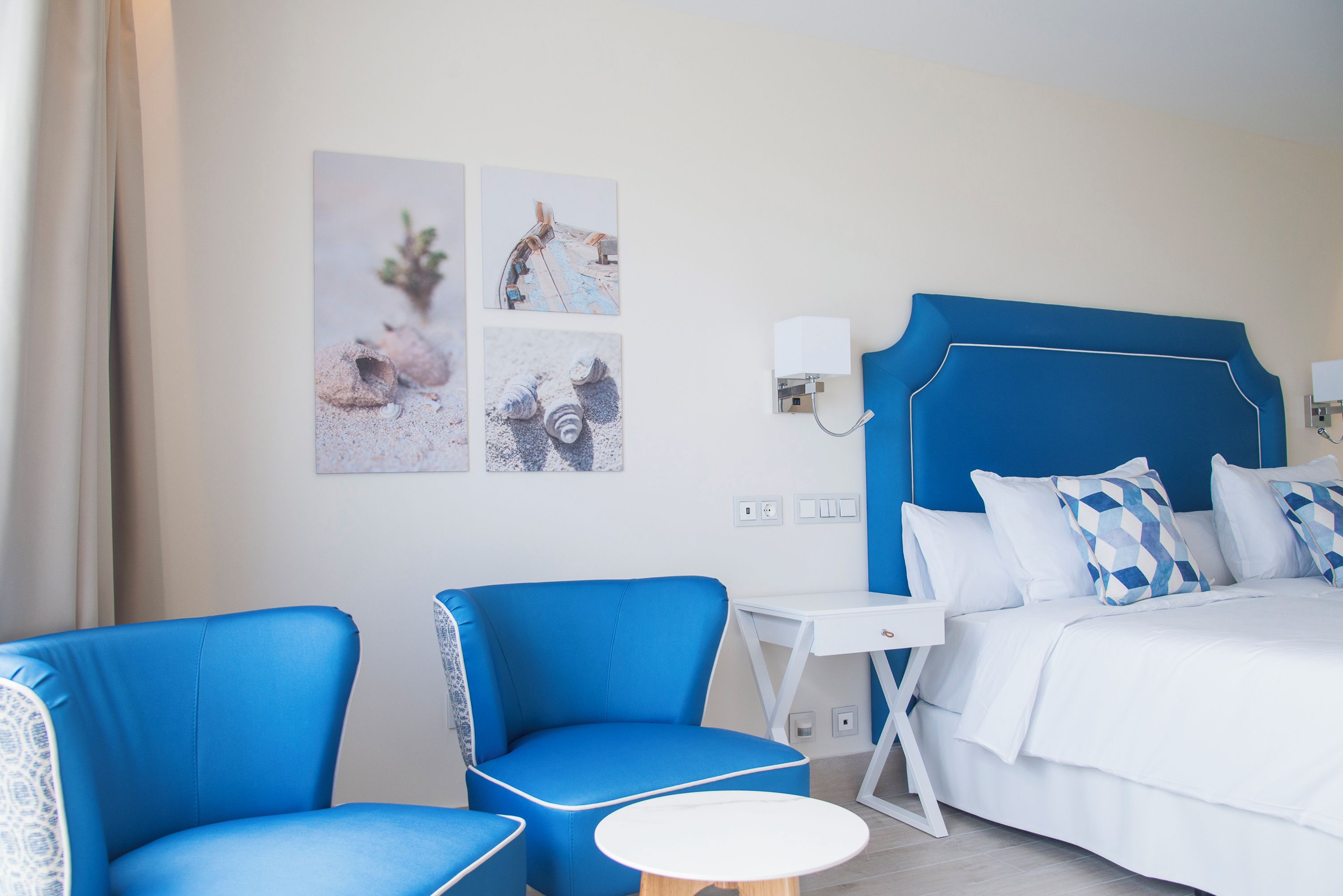Ein Hotelzimmer mit einem Bett, zwei blauen Stühlen, einem kleinen weißen Tisch und Bildern an der Wand.