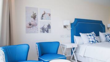 Ein Hotelzimmer mit einem Bett, zwei blauen Stühlen, einem kleinen weißen Tisch und Bildern an der Wand.