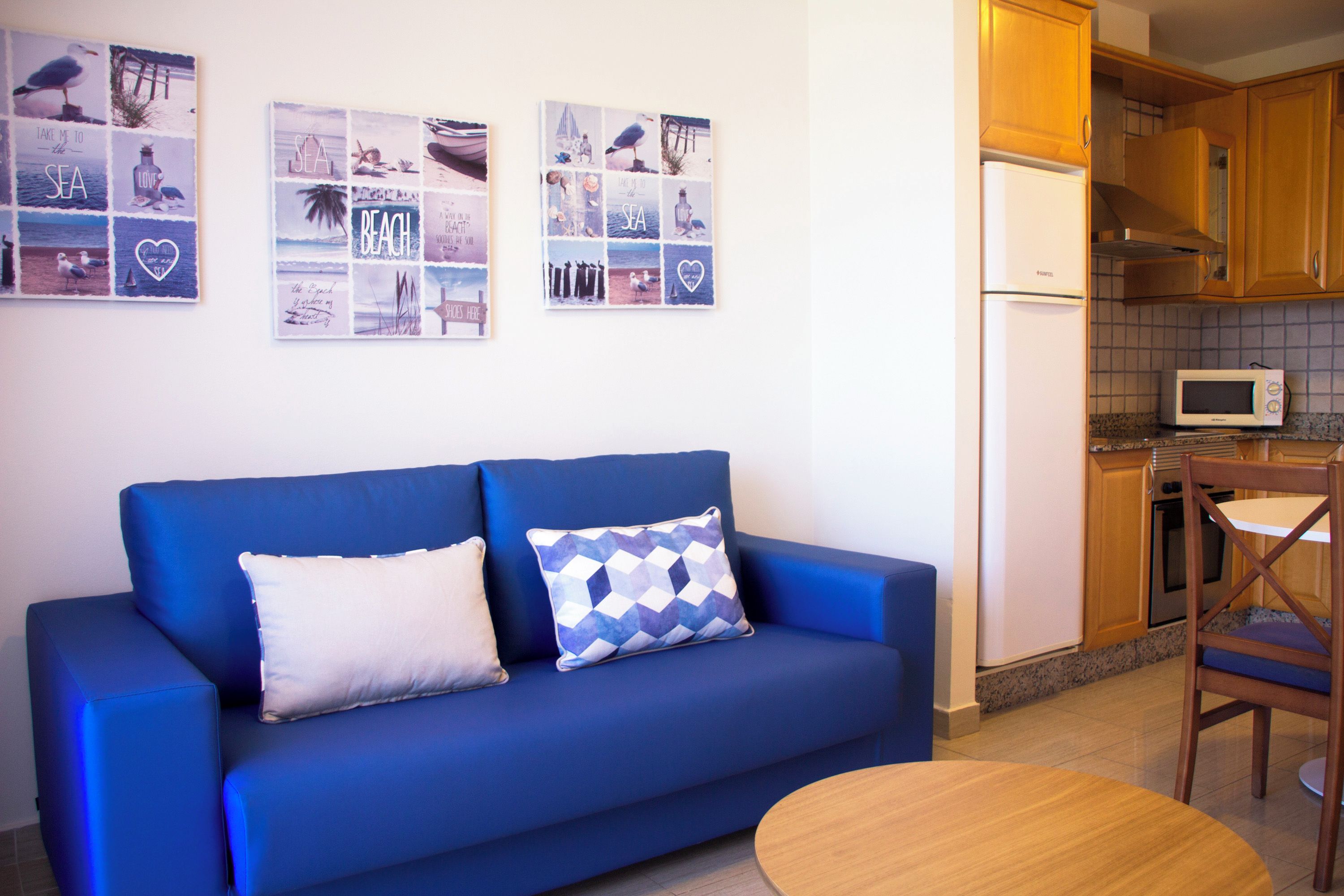 Un sofá azul con dos almohadones, una mesa de comedor de madera y una zona de cocina con microondas.