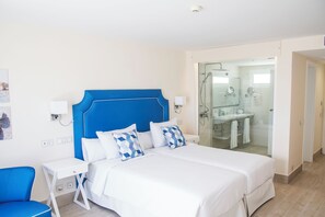 Een hotelkamer met een groot bed, een nachtkastje, een stoel en een badkamer zichtbaar door een glazen deur.