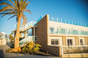 A modern building with a stone facade, glass balconies, and a palm tree in the foreground. - Hotel Boutique Tao Caleta Mar (La Oliva)