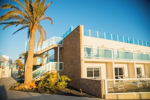 Un edificio moderno con fachada de piedra, balcones de vidrio y una palmera en primer plano.