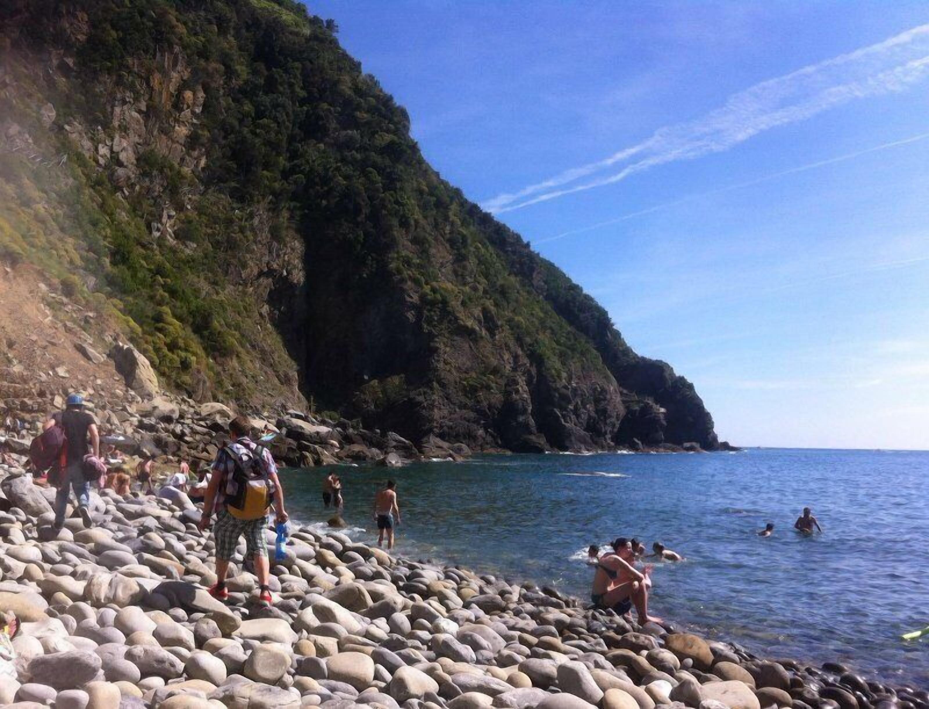 Ein felsiger Strand mit badenden und spazierenden Personen.