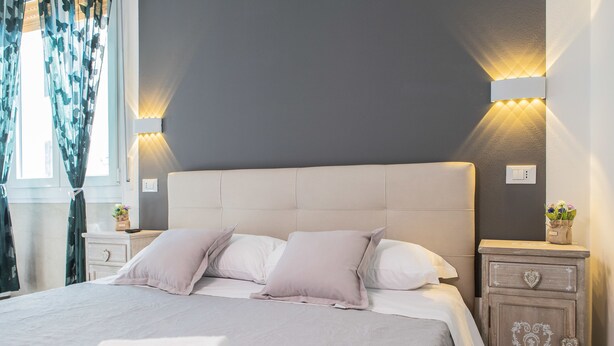 Un lit bien fait, avec une tête de lit blanche, deux tables de chevet avec des lampes et une petite table de nuit dotée d’un tiroir en forme de cœur.