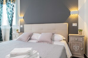 Ein ordentlich bezogenes Bett mit weißem Kopfteil, zwei Nachttische mit Lampen und ein Beistelltisch mit einer schubladenförmigen Herzchen.