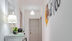 Un couloir avec une console blanche, un miroir et un élément décoratif mural.