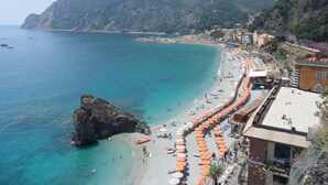 Une ville côtière dotée d’une plage bordée de parasols orange, d’un promontoire rocheux et de bâtiments qui s’étendent le long de la côte.