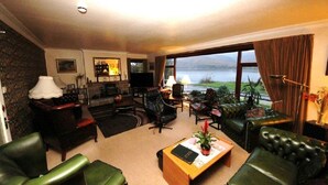 A spacious living room with leather furniture, a coffee table, and a view of a lake. - Stronchreggan View Guest House (Fort William)