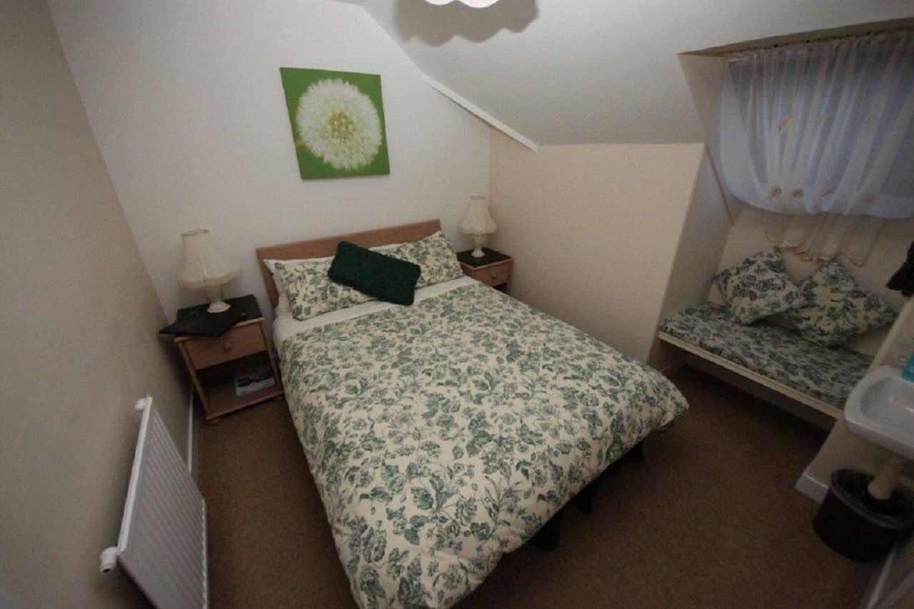 Une chambre à coucher comprenant un lit, deux tables de chevet, une commode, un radiateur, une fenêtre avec des rideaux et un tableau accroché au mur.