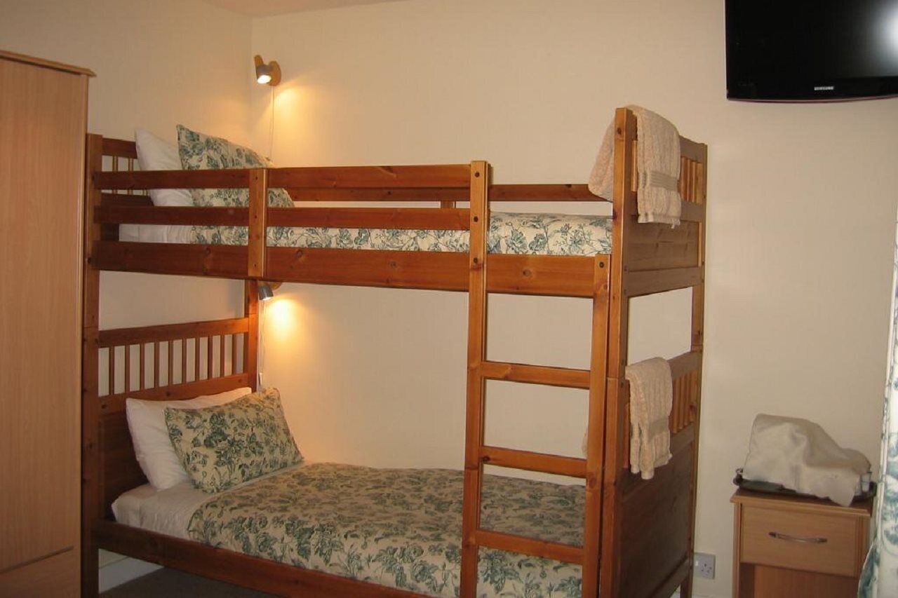 Ein Stockbett mit Holzbettrahmen, ein Nachttisch mit Lampe und ein Fernseher an der Wand.