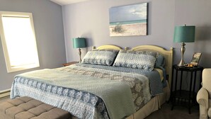 Ein Schlafzimmer mit einem Bett, zwei Nachttischen, einer Bank und einem Bild an der Wand.
