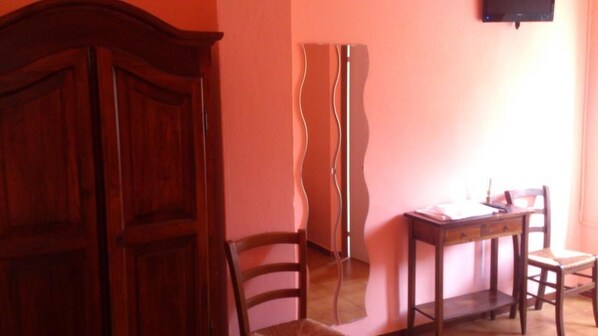 A room with a wooden wardrobe, a desk with a chair, and a mirror on the wall. - Il Piccolo Paradiso (Livorno)