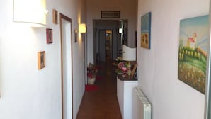 A narrow hallway with a radiator on the right, framed pictures on the left, and a door at the end. - Il Piccolo Paradiso (Livorno)