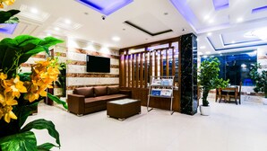 A modern lobby with a sectional sofa, a coffee table, a reception desk, and a large TV screen.